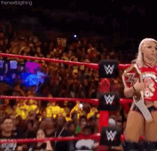 a female wrestler is standing in a wrestling ring holding a trophy .