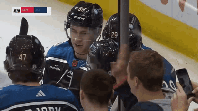 a hockey player with the number 59 on his helmet is surrounded by teammates