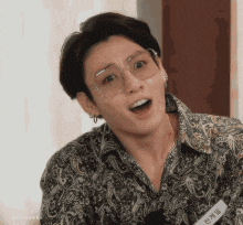 a close up of a man wearing glasses and a paisley shirt making a funny face .