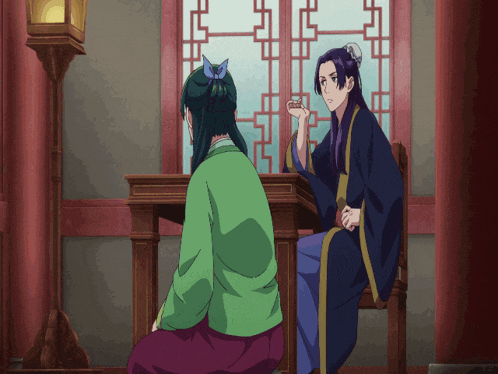 a man in a blue robe sits at a table next to a woman in a green shirt