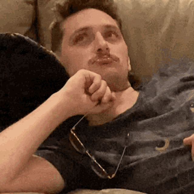 a man laying on a couch wearing glasses and a shirt with the letter o on it