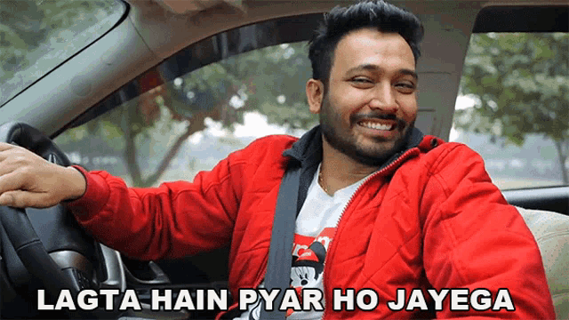 a man in a red jacket is sitting in a car with the words lagta hain pyar ho jayega above him