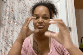 a woman in a pink shirt is making a funny face while cleaning her face with her hands .