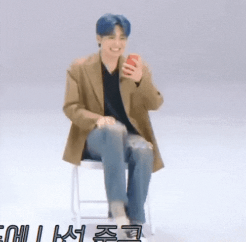 a man is sitting on a stool holding a cell phone and smiling .