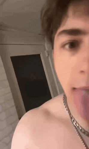a man without a shirt is sticking his tongue out while wearing a chain around his neck .
