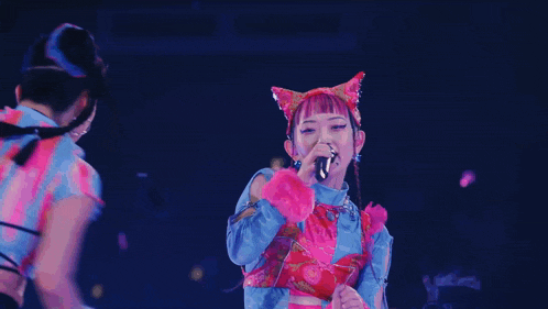 a woman singing into a microphone with a cat ear headpiece