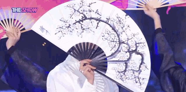 a person holding a fan in front of their face with the show written on the bottom right