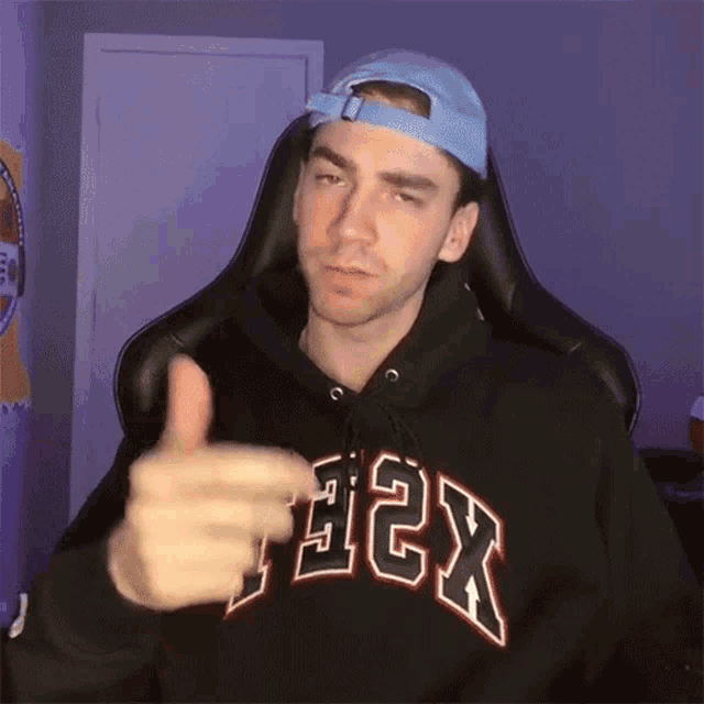 a man wearing a black hoodie and a blue hat is giving a thumbs up sign .