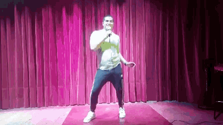 a man is singing into a microphone on stage in front of a pink curtain