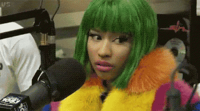 a woman with green hair is wearing a colorful fur coat and talking into a microphone .