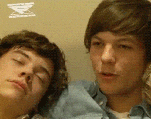 two young men are laying next to each other on a couch .