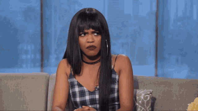 a woman in a plaid top sits on a couch with her eyes closed