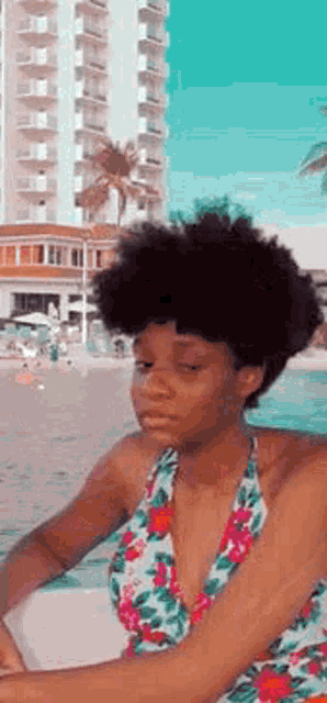 a woman in a floral swimsuit is sitting on a chair on the beach .