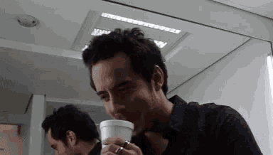 a man is drinking from a styrofoam cup in front of a mirror .