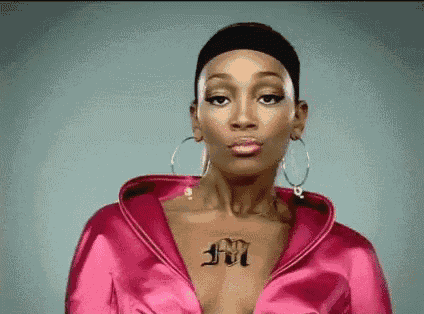a woman wearing a pink jacket and hoop earrings has a tattoo on her chest .