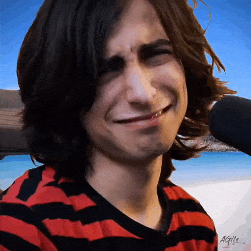 a young man wearing a red and black striped shirt is smiling and making a face