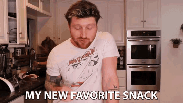 a man in a t-shirt that says " my new favorite snack " is standing in a kitchen