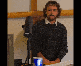 a man in a sweater stands in front of a microphone and a can of red bull