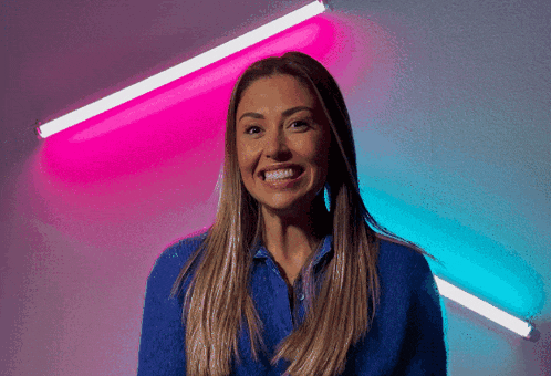 a woman in a blue shirt smiles in front of a pink and blue background