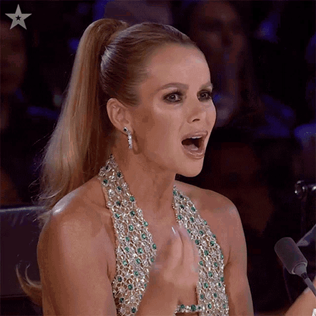 a woman with a ponytail is sitting in front of a microphone with her mouth open .