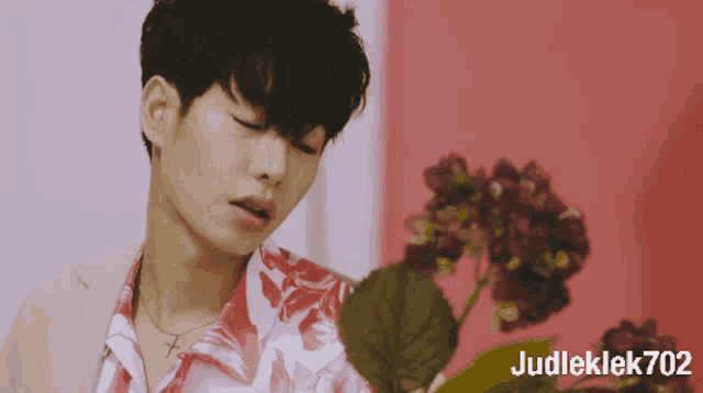 a man in a red and white shirt is holding a flower and the name judleklek702 is on the bottom right