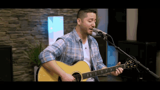 a man in a plaid shirt is singing into a microphone while playing an acoustic guitar