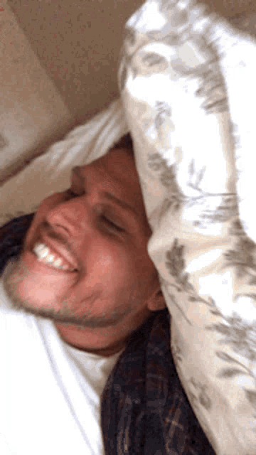 a man in a plaid shirt is smiling while laying in bed