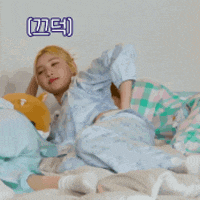 a woman in pajamas is laying on a bed with a stuffed animal behind her