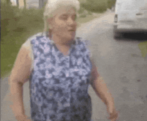 an elderly woman in a blue and purple shirt is standing on a street .