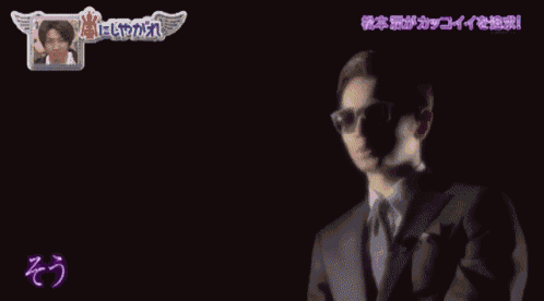 a man wearing sunglasses and a suit is on a tv show in a dark room
