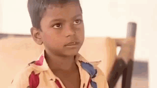 a young boy in a floral shirt is sitting in a chair and looking at the camera .