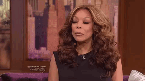 wendy williams is sitting on a couch in front of a painting and making a funny face .