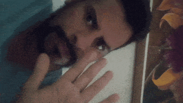 a man with a beard is covering his mouth with his hand in front of a picture of flowers
