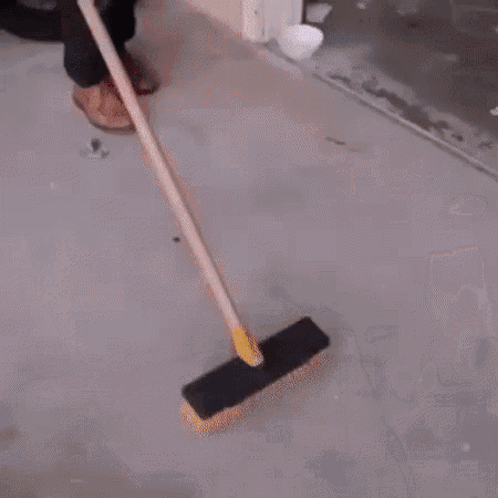 a person is sweeping the floor with a broom in a garage next to a motorcycle .