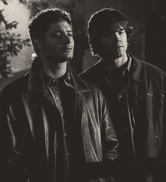 two men in leather jackets are standing next to each other in a dark room