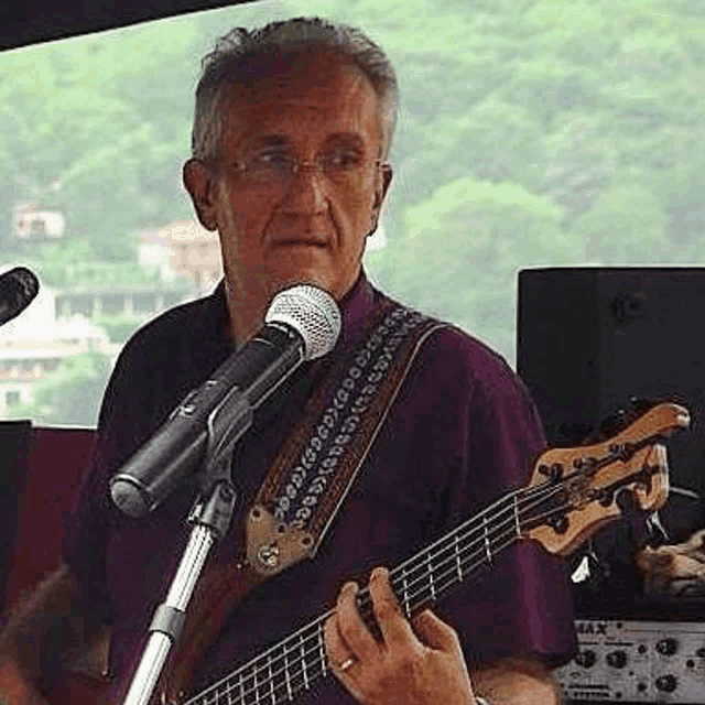 an older man is playing a bass guitar and singing into a microphone .