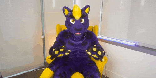 a purple and yellow furry animal is sitting in a yellow chair .