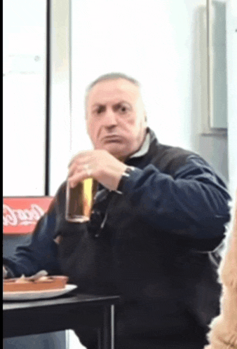 a man is sitting at a table drinking a glass of beer in front of a coca cola sign