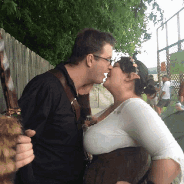 a man and a woman kissing in front of a fence with a sign that says ' a ' on it