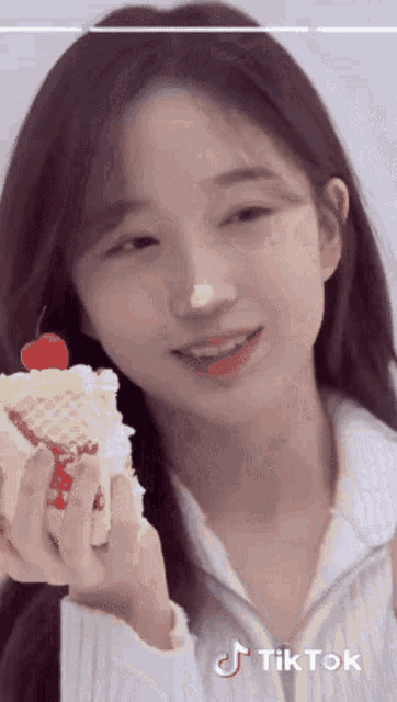 a girl holding a cake with a cherry on top and a tiktok logo on the bottom