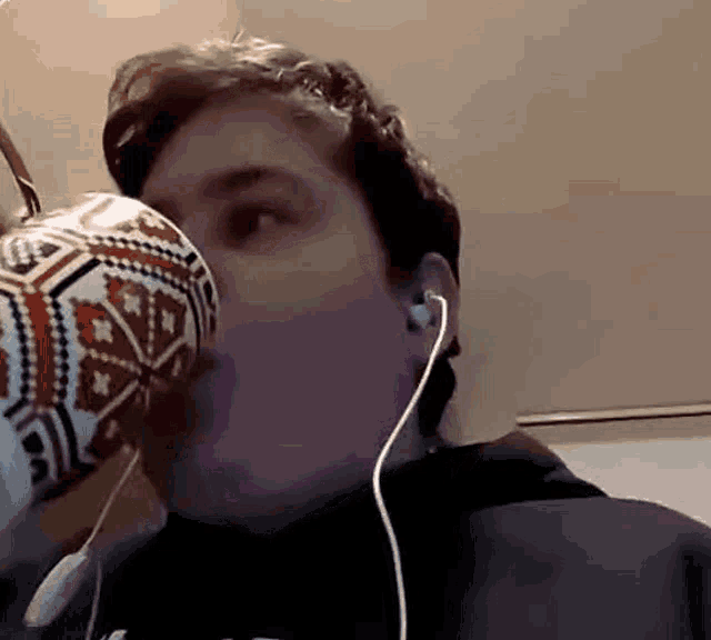 a man wearing headphones is drinking from a mug with a pattern on it