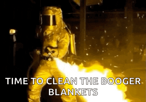 a man in a protective suit is holding a flamethrower in front of a fire .