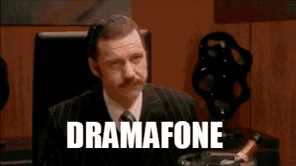 a man in a suit and tie is sitting in front of a sign that says " dramafone " on it
