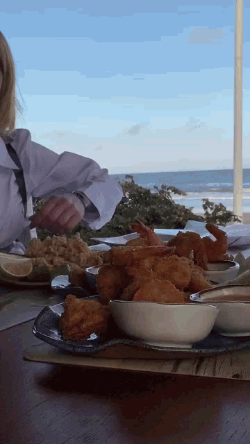 a person is sitting at a table with plates of food and a bowl of shrimp