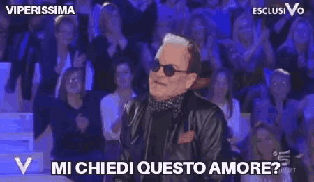 a man wearing sunglasses and a black jacket says " mi chiedi questo amore "