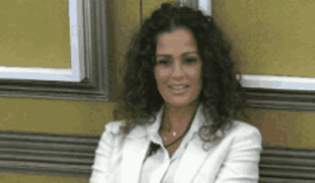a woman with curly hair wearing a white jacket and white shirt