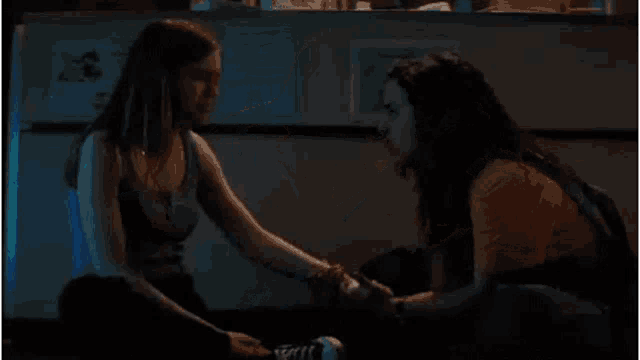two women are sitting on the floor holding hands and looking at each other .