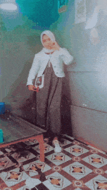 a woman wearing a hijab and a white jacket is standing next to a table
