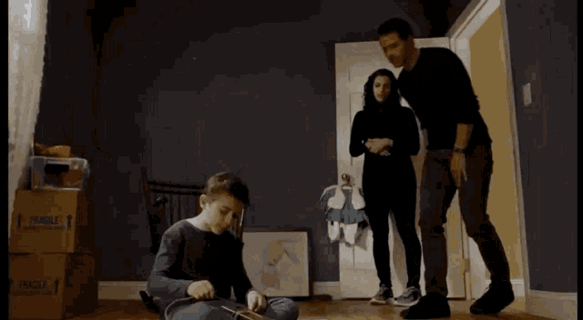 a boy sits on the floor playing with a toy while a man and woman look on