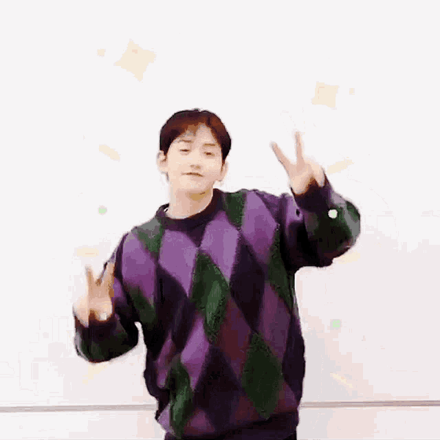 a man wearing a purple and green sweater is giving a peace sign .